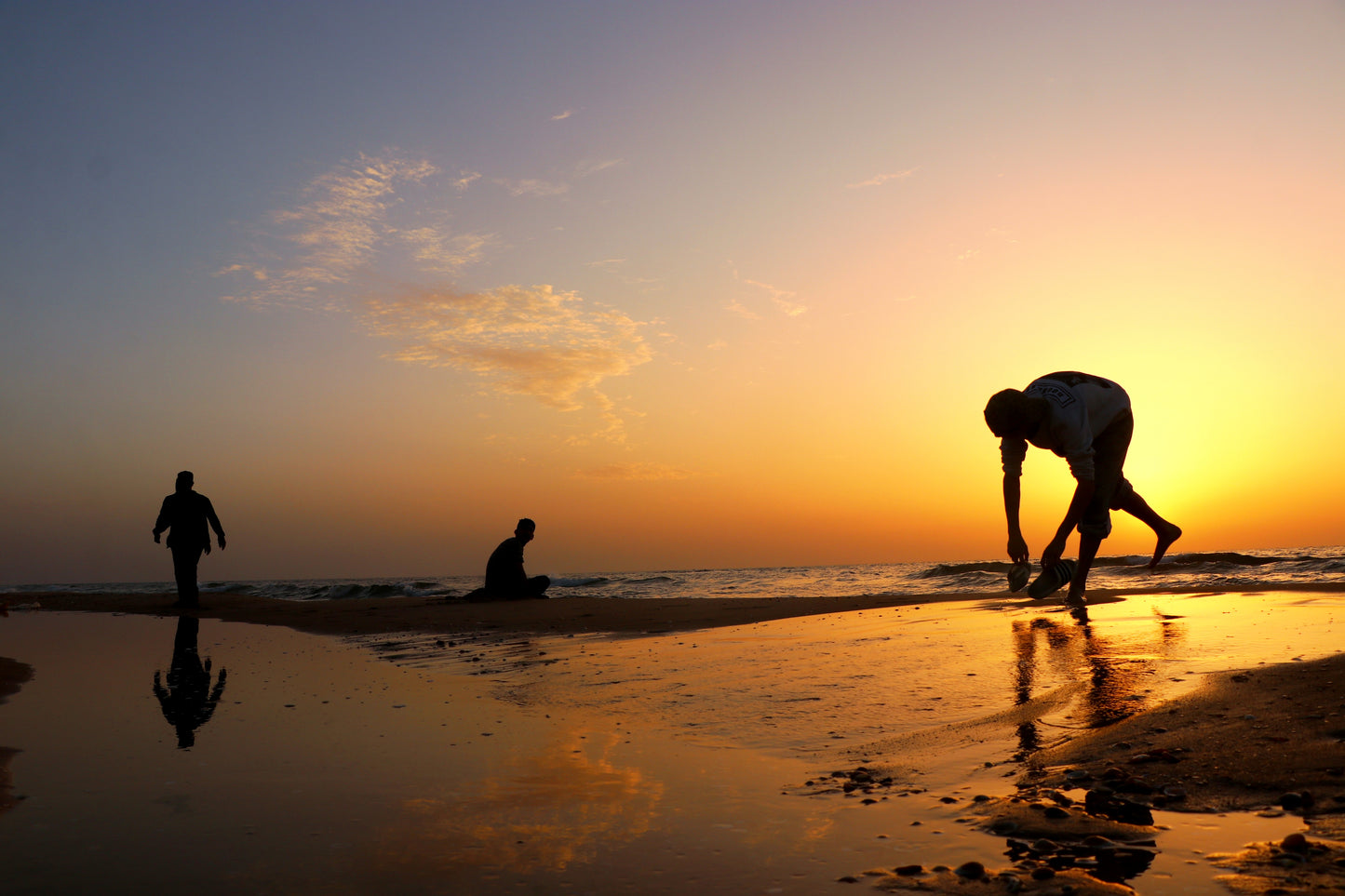 A beautiful photograph of children playing on the beach in Gaza during the sunset colored skies of orange, yellow, blue and purple