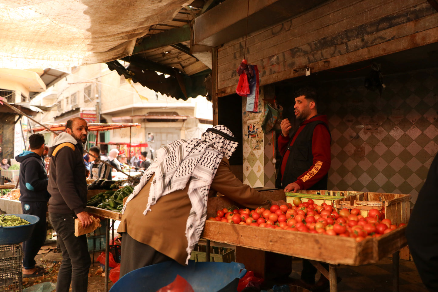 Candid street photograph of a Palestinian marketplace with men exchanging produce, framed by earthy textures and light—capturing daily life and community in Gaza.