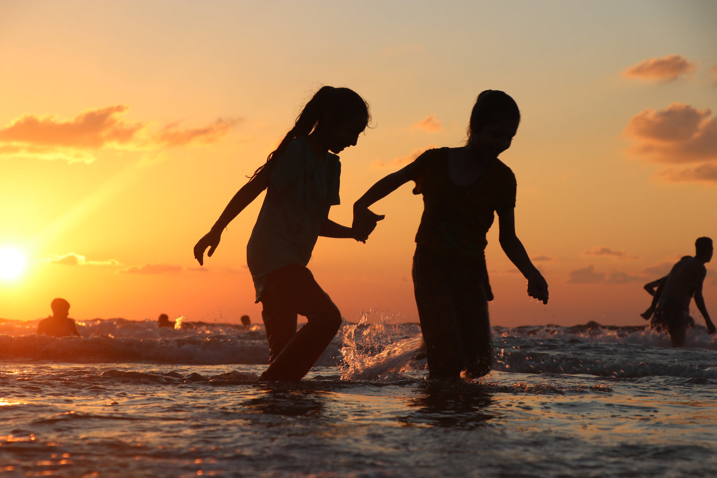Two Palestinian girls holding hands and splashing in Gaza’s sea at sunset, captured by Ibrahim Isam