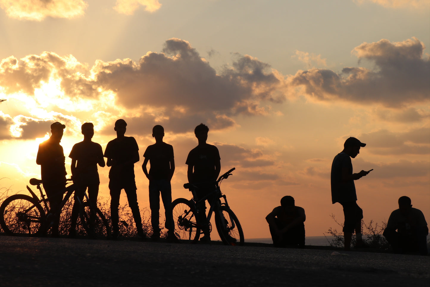 Silhouettes of young Palestinian boys with bikes at sunset in Gaza, captured by Palestinian artist Ibrahim Isam
